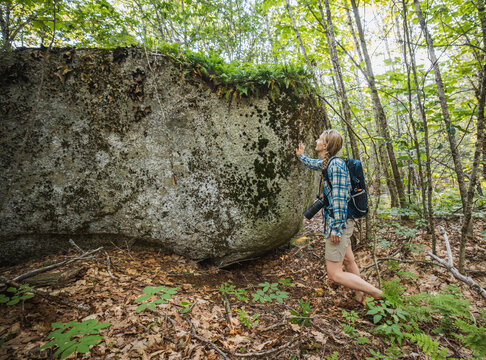 Female hiker and photographer touches a giant mossy boulder