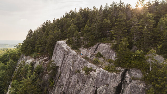 Woman hiking along a steep rocky cliff edge in eastern Maine.