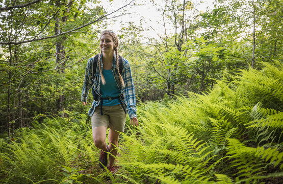 Smiling woman hikes through lush green ferns in forest