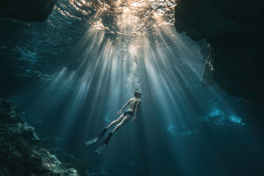 Diver explores underwater cave with sunlight shining through water at midday