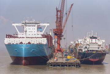 Fototapeta premium New ships berthed at a shipyard during the final phase of vessel completion, with the vessels being prepared for departure and their first voyage.