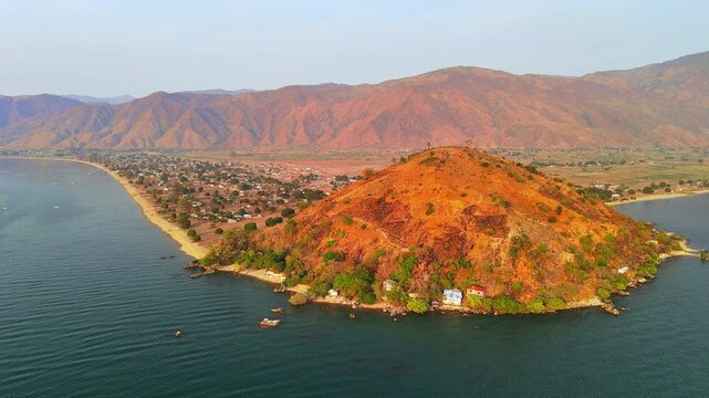Aerial view of Usisya Village beyond its distinctive lakeside hill, with scattered homes and reddish mountains rising across the background.