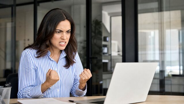 Frustrated businesswoman clenching fists at laptop in office