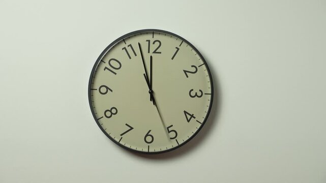 Black wall clock with moving hands in a time lapse, mounted on a white wall and showing twelve o'clock. Timelapse of a classic wall clock with running time pointers and a clean minimalist background.