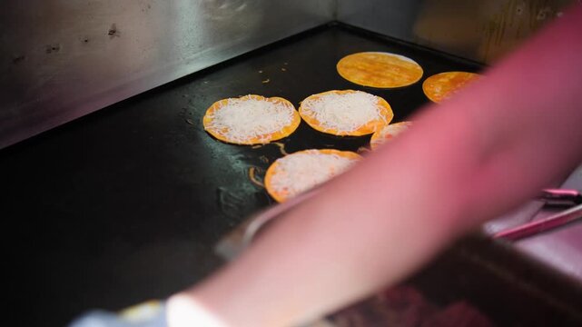 A cook dips corn tortillas into rich red birria consome before grilling them for traditional Mexican quesabirria tacos