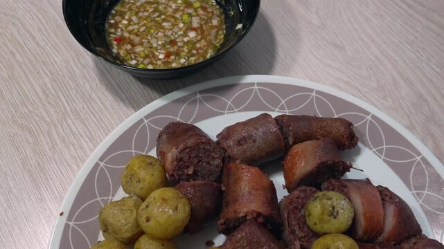 Cooked morcilla slices and seasoned baby potatoes sit on a plate beside a bowl of chopped aji dipping sauce on a wooden table.