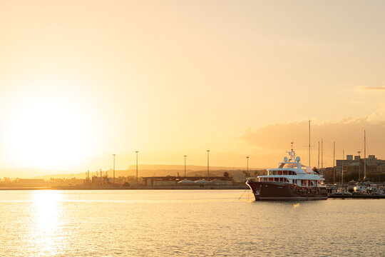 A magnificent yacht rests peacefully on calm waters as the sun dips below the horizon, casting a warm, serene glow over the bay