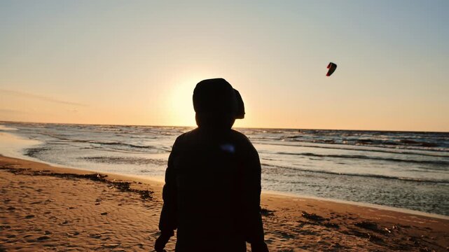 Silhouette opens arms toward a golden sea sunset as kite surfers move offshore