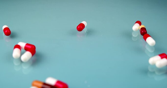 Close up view of multi colored red, white, orange, and brown medicine capsules falling on a light blue glass surface, clinical health therapy and pharmacy drug concept