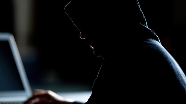 Anonymous hacker in a dark room using a laptop for cybercrime and data breach