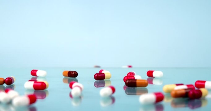 Red and white, orange and brown medical pills and capsules falling onto a light blue glass table surface in slow motion, pharmacy drug treatment and healthcare addiction concept layout