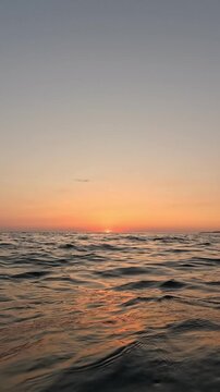 Scenic golden hour over calm ocean waters with glowing orange reflections on gentle waves. Vertical handheld shot.