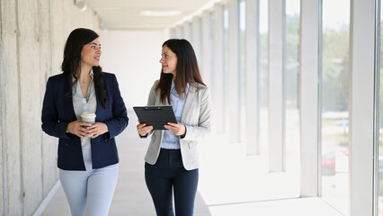 Obraz premium Businesswomen walking and discussing corporate partnership in office hallway
