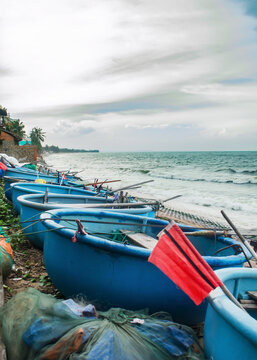 Vietnamese round basket boats lined on beach shore with waves. Blue traditional coracle fishing boats for maritime culture, travel and fishing industry concept.