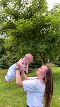 Happy mother lifts her baby into the air while playing outdoors, joyful parenthood, family bonding and playful summer childhood moment.