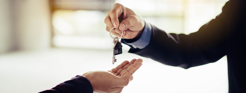 close up view hand of property realtor landlord giving key house to buyer tenant.