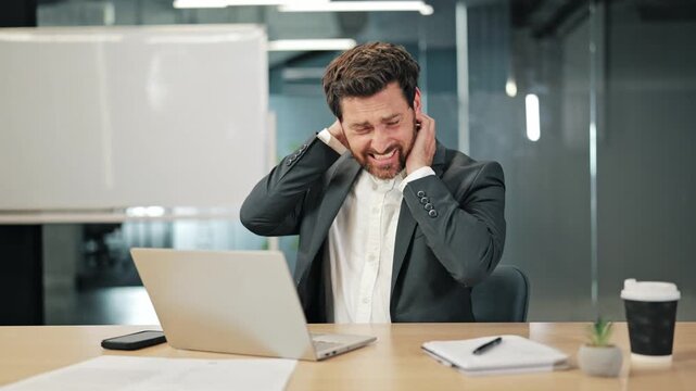 Businessman works on laptop, experiences wrist and neck pain, then becomes frustrated. Long hours and stress lead to discomfort and anger in office setting.