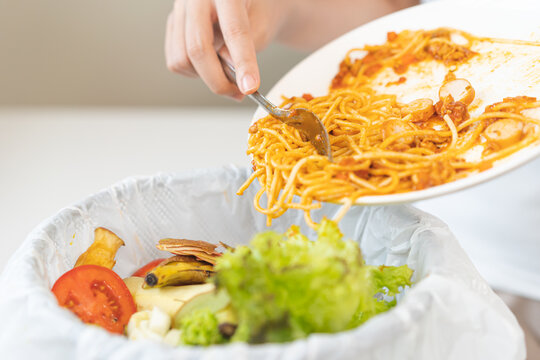 Compost from leftover food asian young housekeeper woman, female hand holding spaghetti plate use fork scraping waste, food throwing away into garbage, trash or bin. Environmentally responsible.