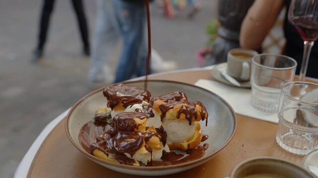 Chocolate sauce poured over profiteroles and vanilla ice cream at a Paris cafe