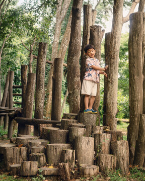 A young child exploring and climbing a natural wooden playground surrounded by trees, enjoying outdoor adventure, physical activity, and imaginative play in nature.