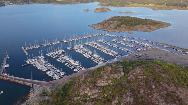 Aerial view of Sando marina in Vallda, featuring numerous sailboats docked in rows, surrounded by rocky coastline and calm blue water in Vallda, Hallands lan, Sweden.