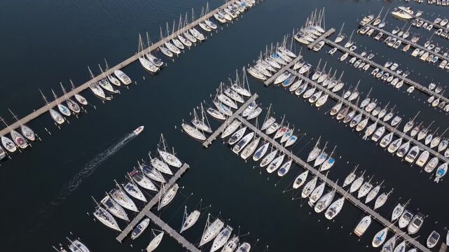 Aerial view of Sando marina featuring numerous sailboats docked in rows and a small motorboat moving through the calm water in Vallda, Hallands lan, Sweden.