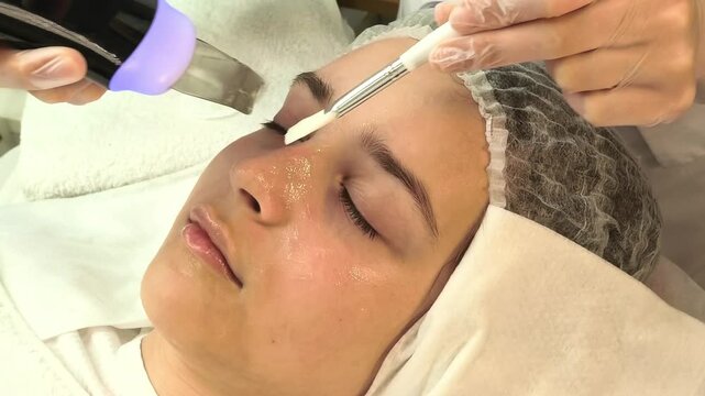 Esthetician performs ultrasonic facial cleansing on a teenage girl in a beauty salon, professional skincare, exfoliation and pore purification.