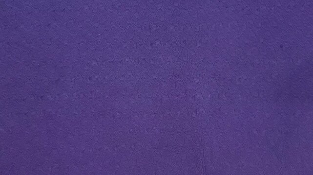A hand moves a small purple massage ball across a purple exercise mat, self massage practice, mobility exercise, wellness routine.