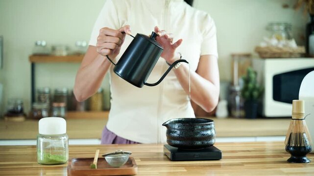 Woman Pouring Hot Water from Gooseneck Kettle into Matcha Bowl During Traditional Tea Ceremony Preparation