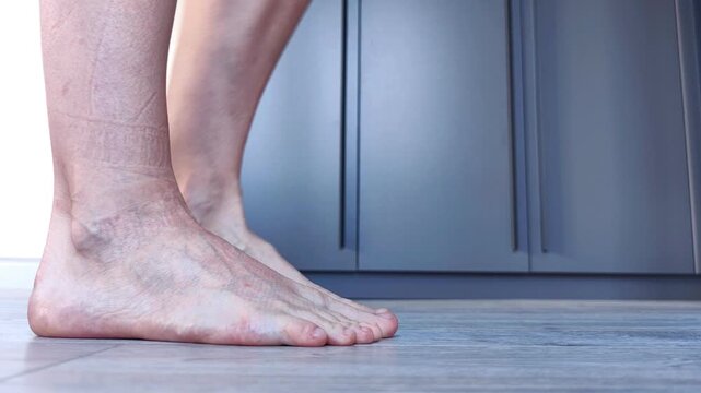 A close-up shows an adult woman bare foot  alternately lifts her bare feet onto the balls of her feet, foot massage and mobility exercise.