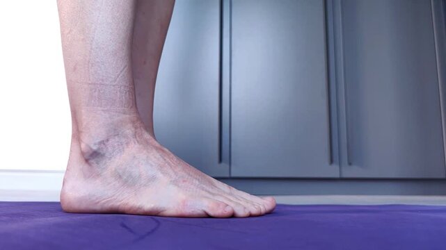A close-up of a woman's bare feet squeezing a small massage ball between her ankles and rising onto tiptoes, foot health, balance, mobility and body awareness concept.