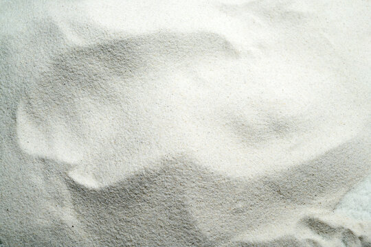 An overhead view of fine white sand showing natural wavy ripple patterns, creating a clean, minimalist texture. Summer, natural or texture background