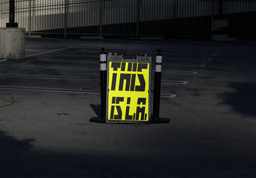 Mockup of A blank A-frame sign is placed in a parking lot in Los Angeles. The area is empty with clear markings showing parking spaces.