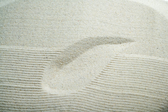 Close-up of raked white sand with a smooth curved stroke, representing mindfulness, Zen philosophy, and peaceful meditation. Summer, natural or texture background
