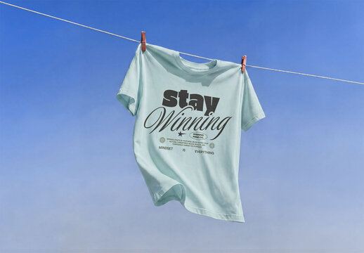 Mockup of A simple green t-shirt is hanging on a line in the open air. The blue sky serves as a backdrop. It is a sunny day.