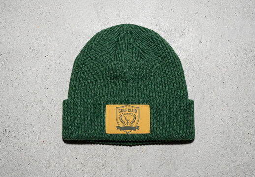 Mockup of A green beanie cap is placed flat on a gray concrete surface. The beanie features a blank label for customization.