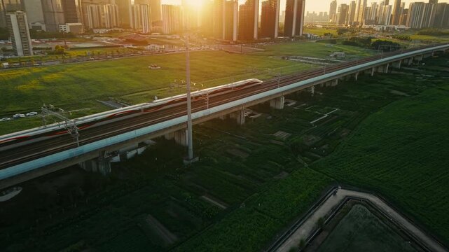 Aerial view of a high speed train travels on an elevated track past tall apartment buildings in a city suburb during sunset in China