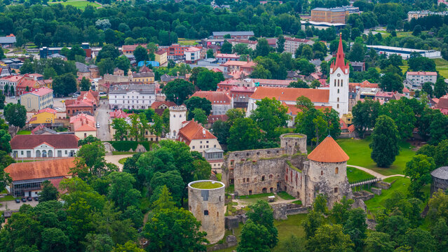 drone shot showing Cesis Castle ruins in the foreground and St John Church tower emerging above green trees in Cesis, Latvia
