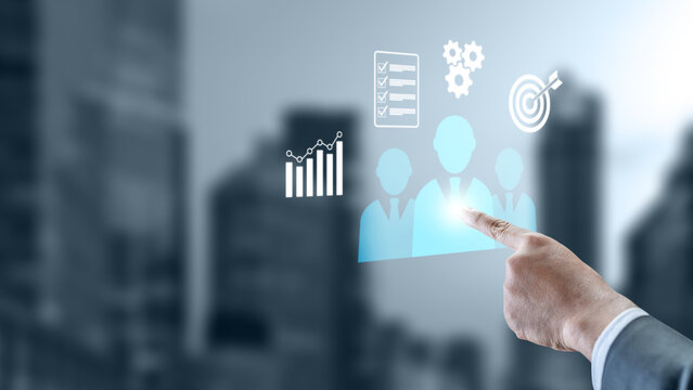 Businessman pointing at virtual icons representing human resources, team management, target, and business growth on a blurred office background. Management concept