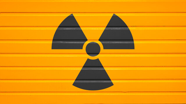 Black radiation warning symbol painted on a bright yellow metal shutter background. Nuclear concept