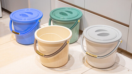 Plastic buckets stand on a tiled floor. © Bima