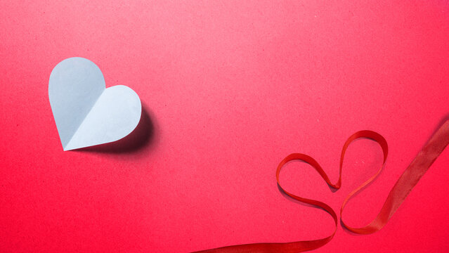 White paper heart and red ribbon shaped like a heart on a textured red background. Minimalist Valentine's Day craft concept with copy space. Happy Sweetest Day Concept