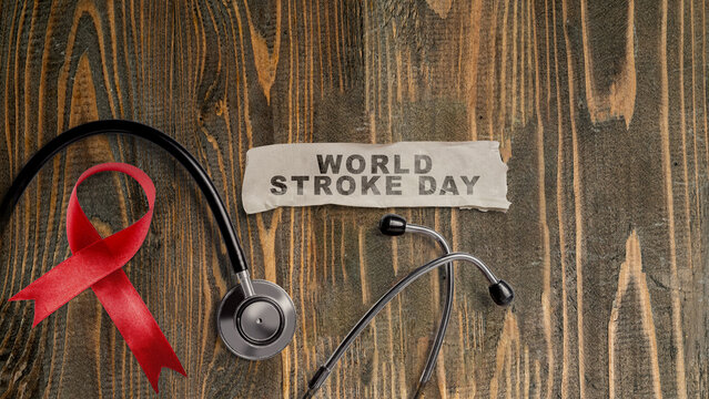 World Stroke Day concept with a stethoscope, red ribbon, and text on a torn paper over a wooden background. World Stroke Day Awareness Campaign Concept
