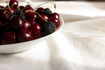 Macro shot of fresh ripe sweet cherries and blackberries in a bowl under bright sunlight with natural shadows. © Svetlana