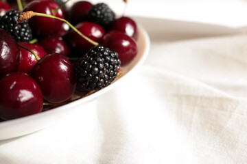 Macro shot of fresh ripe sweet cherries and blackberries in a bowl under bright sunlight with natural shadows. © Svetlana