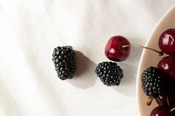 Macro shot of fresh ripe sweet cherries and blackberries in a bowl under bright sunlight with natural shadows. © Svetlana