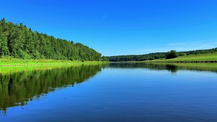 Obraz premium Serene river reflecting lush green forests under a clear blue sky in summer essence