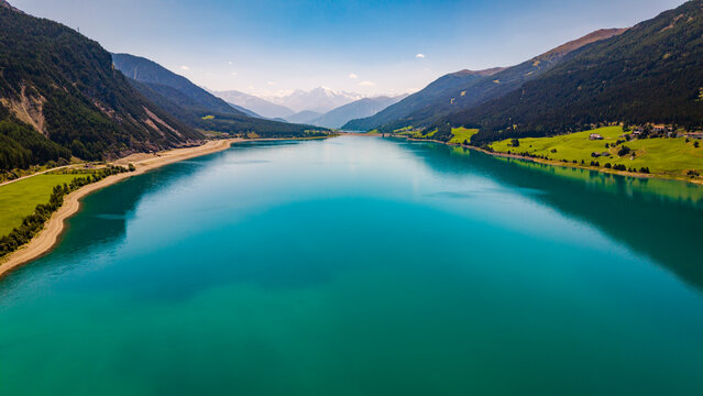 Aerial panorama overlooking the vibrant turquoise waters of Lake Resia stretching through the alpine valley in South Tyrol, Italy.