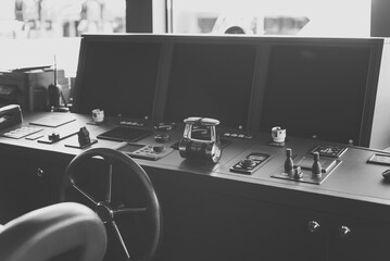 Black and white photo of wheelhouse, bridge of a modern new build superyacht, with wooden wheel, throttle controls, radar, auto-pilot, navigation and other control panels © lupiphoto