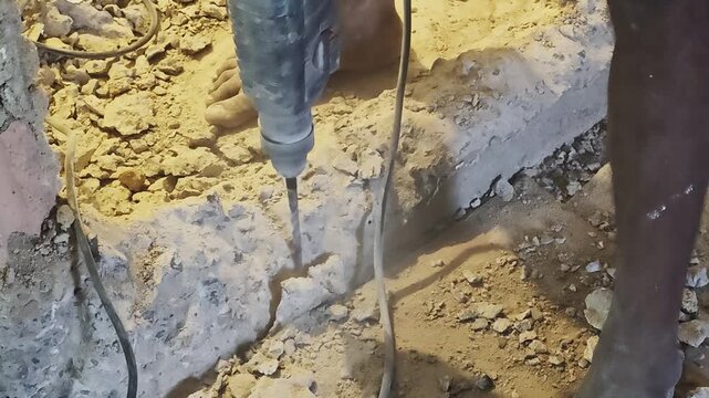 a high power electric rotary hammer drill chipping and drilling through a solid concrete stone wall on a construction site. High impact power tool creating heavy dust debris during home renovation
